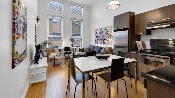 A modern kitchen with a dining area, large windows, and artwork on the walls. - LiV MTL Main Plateau Urban Suites Near Downtown Montreal (Montréal)