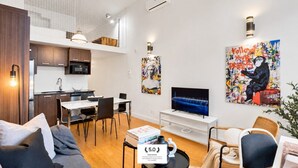 A modern living room with a sofa, dining table, and TV. There's a kitchen area with cabinets and a microwave. Artwork is displayed on the walls. - LiV MTL Main Plateau Urban Suites Near Downtown Montreal (Montréal)