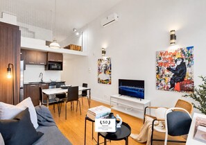 A modern living room with a sofa, dining table, and TV. There's a kitchen area with cabinets and a microwave. Artwork is displayed on the walls. - LiV MTL Main Plateau Urban Suites Near Downtown Montreal (Montréal)