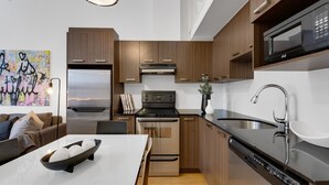A modern kitchen with wooden cabinets, stainless steel appliances, and a white countertop. - LiV MTL Main Plateau Urban Suites Near Downtown Montreal (Montréal)