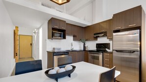 A modern kitchen with wooden cabinets, stainless steel appliances, and a dining area with a white table and blue chairs. - LiV MTL Main Plateau Urban Suites Near Downtown Montreal (Montréal)