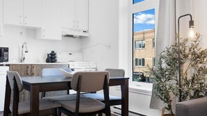 A modern kitchen with white cabinets, a dining table with chairs, a stove, and a window with a view of a building. - LiV MTL MTL Plateau Urban Suites Near Downtown Montreal (Montréal)