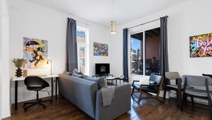 A modern living room with a grey sofa, a black office chair, a TV, and artwork on the walls. - LiV MTL MTL Plateau Urban Suites Near Downtown Montreal (Montréal)