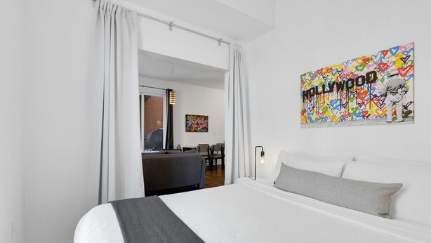 A hotel room with a large bed, a desk, and a chair. There is a painting on the wall and a window with curtains. - LiV MTL MTL Plateau Urban Suites Near Downtown Montreal (Montréal)