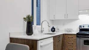 Une cuisine moderne avec des meubles blancs, une cuisinière en acier inoxydable, un évier et une petite plante en pot.