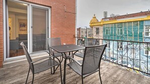 Un balcon avec une table et des chaises, une porte-fenêtre coulissante et une vue sur un bâtiment doté d’un dôme jaune et d’une façade verte.