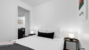 Une chambre d’hôtel au décor minimaliste, avec un lit, des tables de chevet et un tableau au mur.