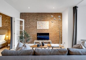 Un salon moderne avec un mur en briques, un téléviseur à écran plat, un canapé, une table basse et une table d’appoint agrémentée d’objets décoratifs.