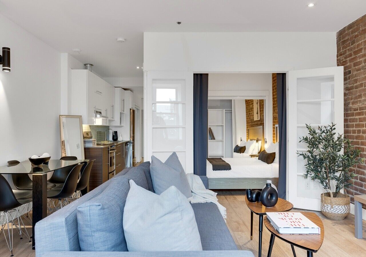 A modern living room with a sofa, dining table, and kitchen in the background.