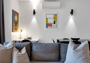 A modern living room with a grey sofa, two wall-mounted lights, an air conditioning unit, and a framed abstract artwork. - Spacious Downtown 2BR • Sleeps 6 (Montréal)