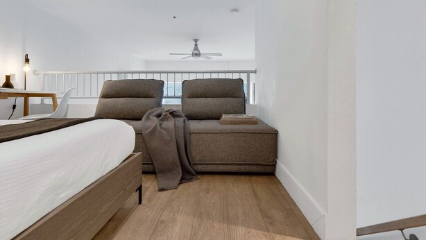 Une chambre à coucher moderne, avec un lit, deux fauteuils, une petite table et un ventilateur de plafond.