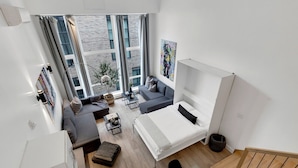 Eine moderne Wohnung mit Bett, Sofa, Essbereich, großen Fenstern und Blick auf die Stadt.