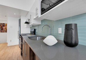 A modern kitchen with a grey countertop, stainless steel sink, and a black vase. - Downtown Duplex Mezzanine • Sleeps 8 (Montréal)
