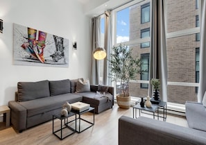 Un salon moderne avec un canapé gris, une table basse et une grande fenêtre avec des rideaux.