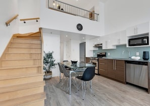 A modern kitchen with a dining area, wooden staircase, and a view to the upper floor.