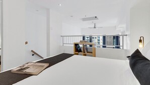 A modern hotel room with a large bed, a small desk, a bookshelf, and a view of the city through the window.