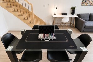 Un salon moderne avec une table à manger au plateau en verre, des chaises noires, un escalier, un bureau blanc avec une lampe et un canapé gris.