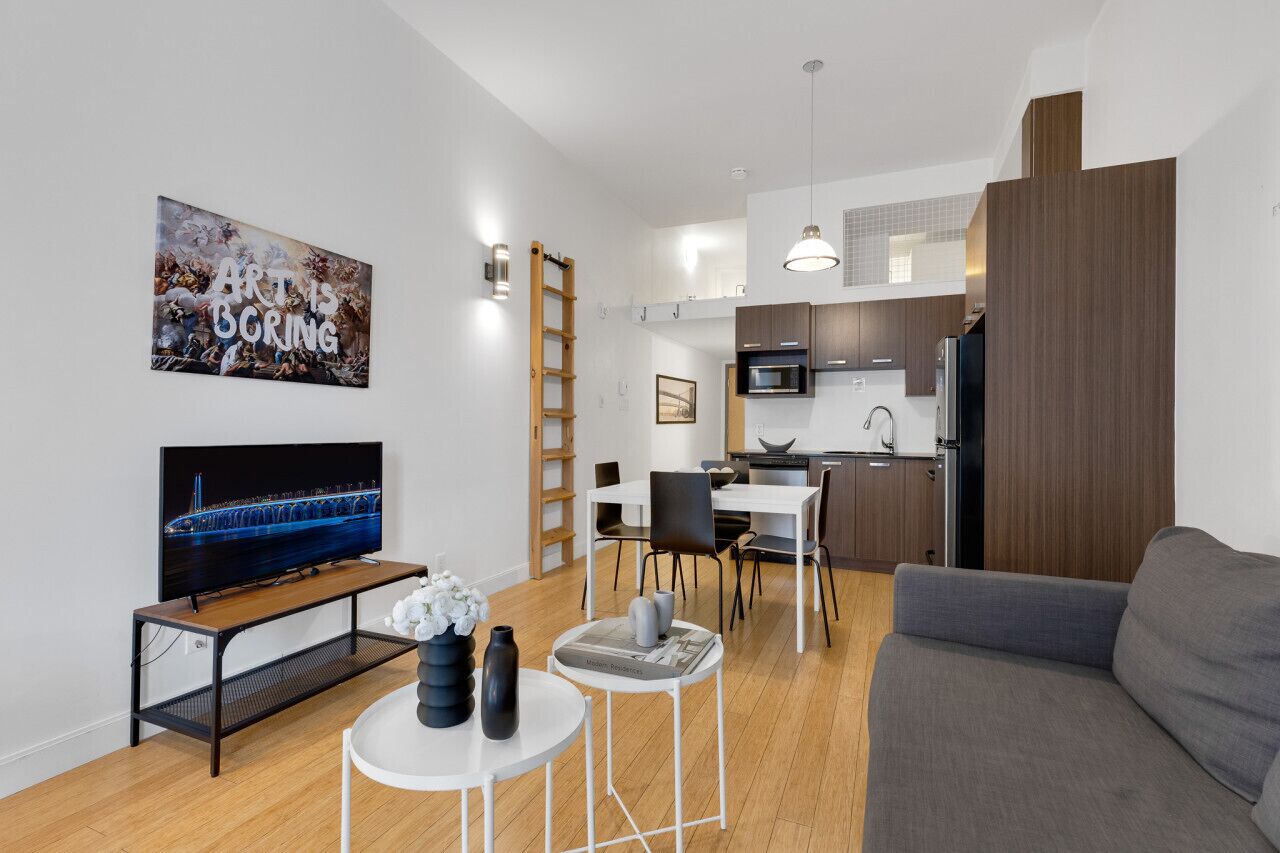 A modern living room with a flat-screen TV, a sofa, a coffee table, and a dining area with chairs and a small table.