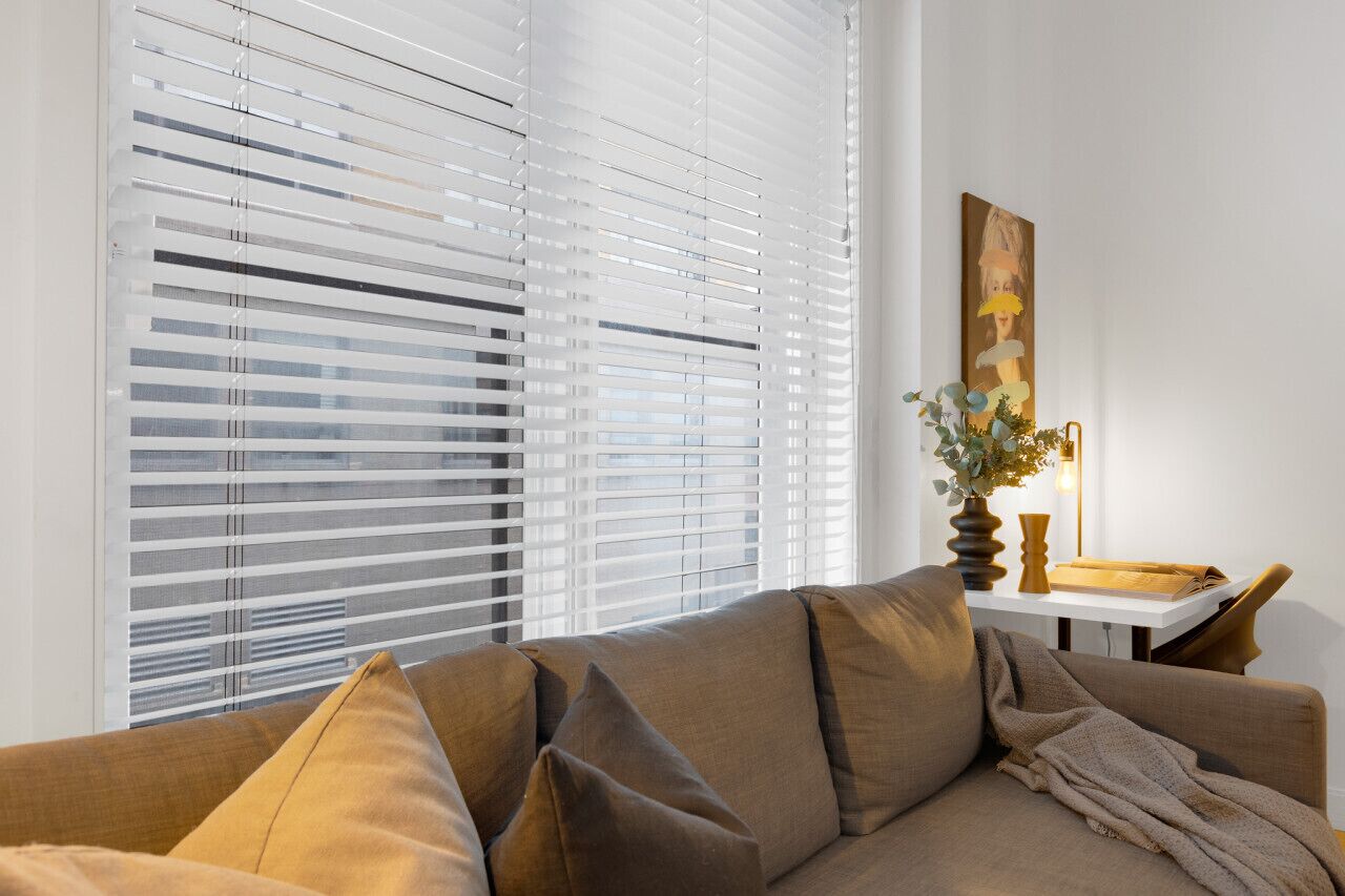 Een woonkamer met een bank, een tafel met een vaas en een lamp, en een schilderij aan de muur.