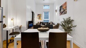 Moderni keittiö, jossa on valkoiset kaapit, ruokapöytä tuoleineen, suuri ikkuna ja seinällä taulu.