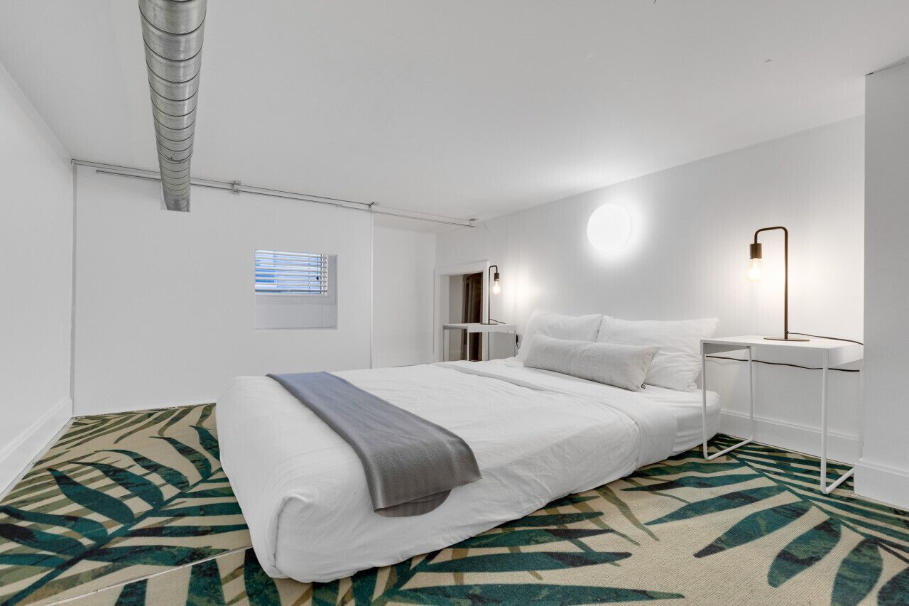Een moderne hotelkamer met een groot bed, een nachtkastje, een lamp en een raam met jaloezieën.