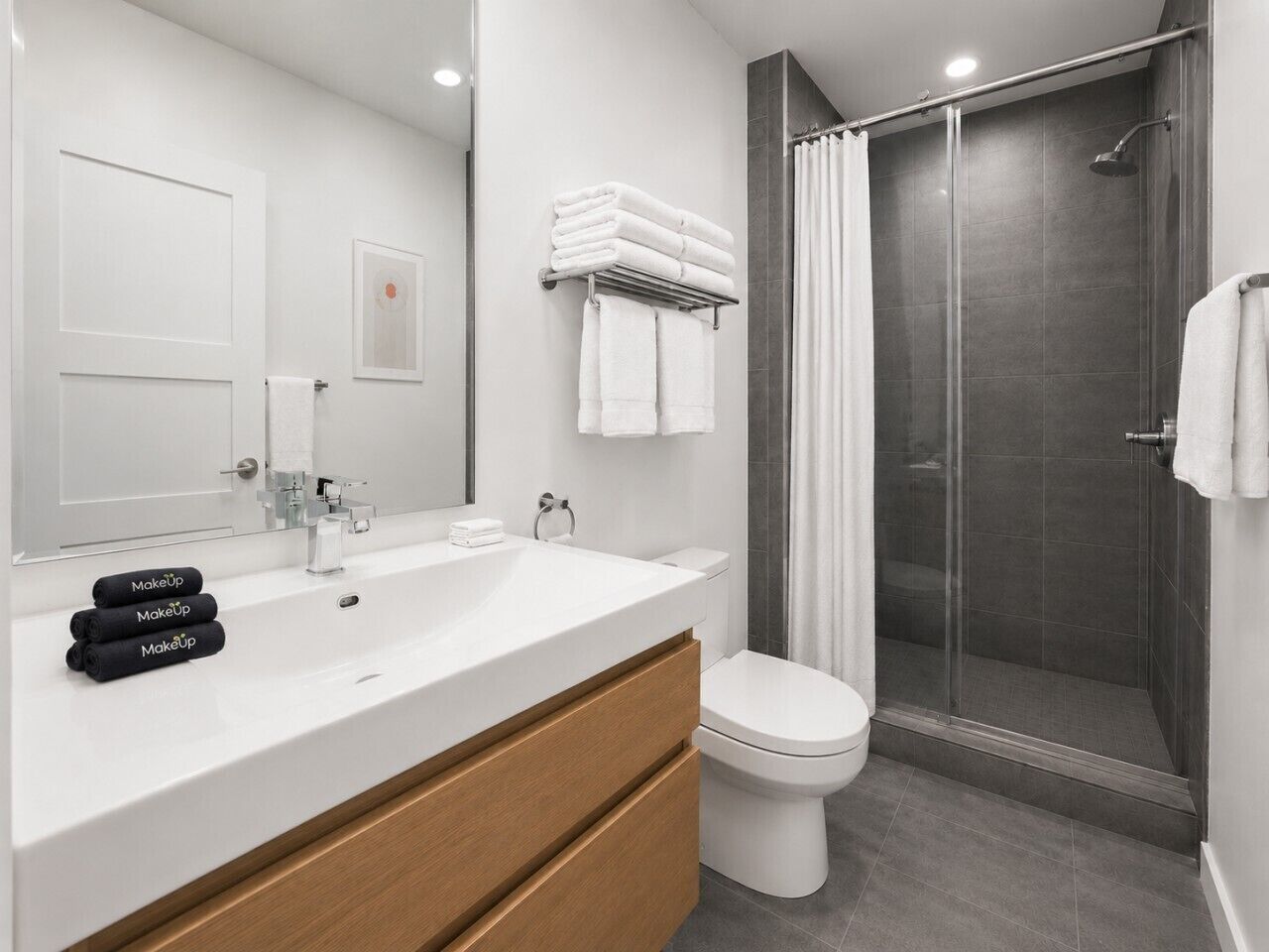 A modern bathroom with a white sink, a toilet, a shower with a glass door, and a mirror.