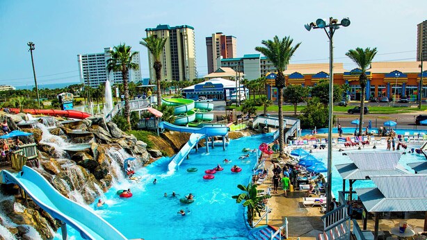 Un parque acuático con múltiples toboganes y piscinas, rodeado de palmeras y edificios urbanos.