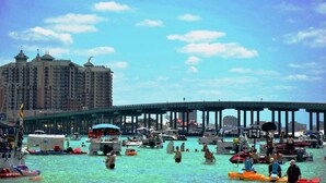 Un paseo marítimo animado con barcos y gente en el agua, un hotel grande al fondo, y un muelle que se adentra en el agua.