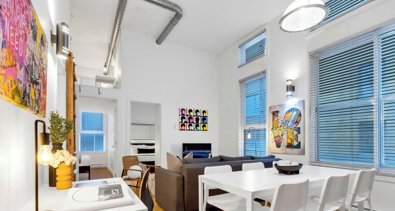 Ein modernes Wohnzimmer mit Sofa, Esstisch und Stühlen. Ein Fernseher, Kunstwerke an der Wand und ein Fenster mit Jalousien sind ebenfalls vorhanden.
