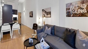A modern living room with a grey sofa, white chairs, a dining table, and artwork on the walls.