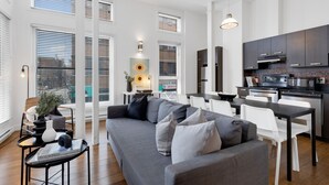 Un apartamento moderno con un sofá gris, sillas blancas y una zona de cocina.