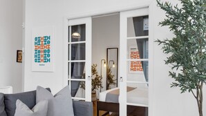 Una sala moderna con un sofá gris, una cama con cabecera blanca y un ventanal grande.