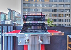 Een draagbare grill op een balkon, met een stadsgezicht op de achtergrond.