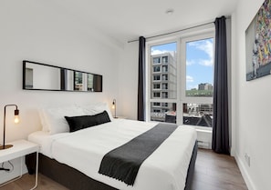 A modern hotel room with a large bed, a bedside table with a lamp, a window with curtains, and a city view. - Spacious 3BR Penthouse Rooftop • Sleeps 12 (Montréal)