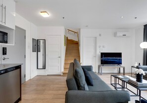 Een moderne woonkamer met een grijze bank, een flatscreen televisie en een trap naar een hoger niveau.