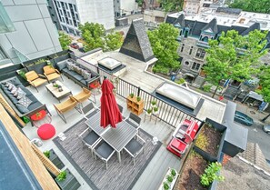 A rooftop terrace with outdoor seating, a red umbrella, and a view of the cityscape. - Spacious 3BR Penthouse Rooftop • Sleeps 12 (Montréal)