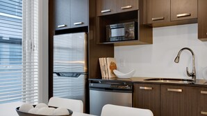 A modern kitchen with dark wood cabinets, a stainless steel refrigerator, a built-in microwave, a sink with a modern faucet, and a dining area with a white table and chairs.