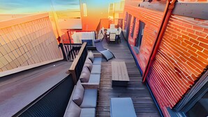 Una terraza en la azotea con una larga hilera de asientos acolchados, una mesita y vistas al atardecer.