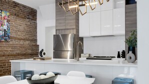 A modern kitchen with a stainless steel refrigerator, white cabinets, and a brick wall accent. - LiV MTL Soho Spacious Rooftop Suites for Groups Near Downtown Montreal (Montréal)