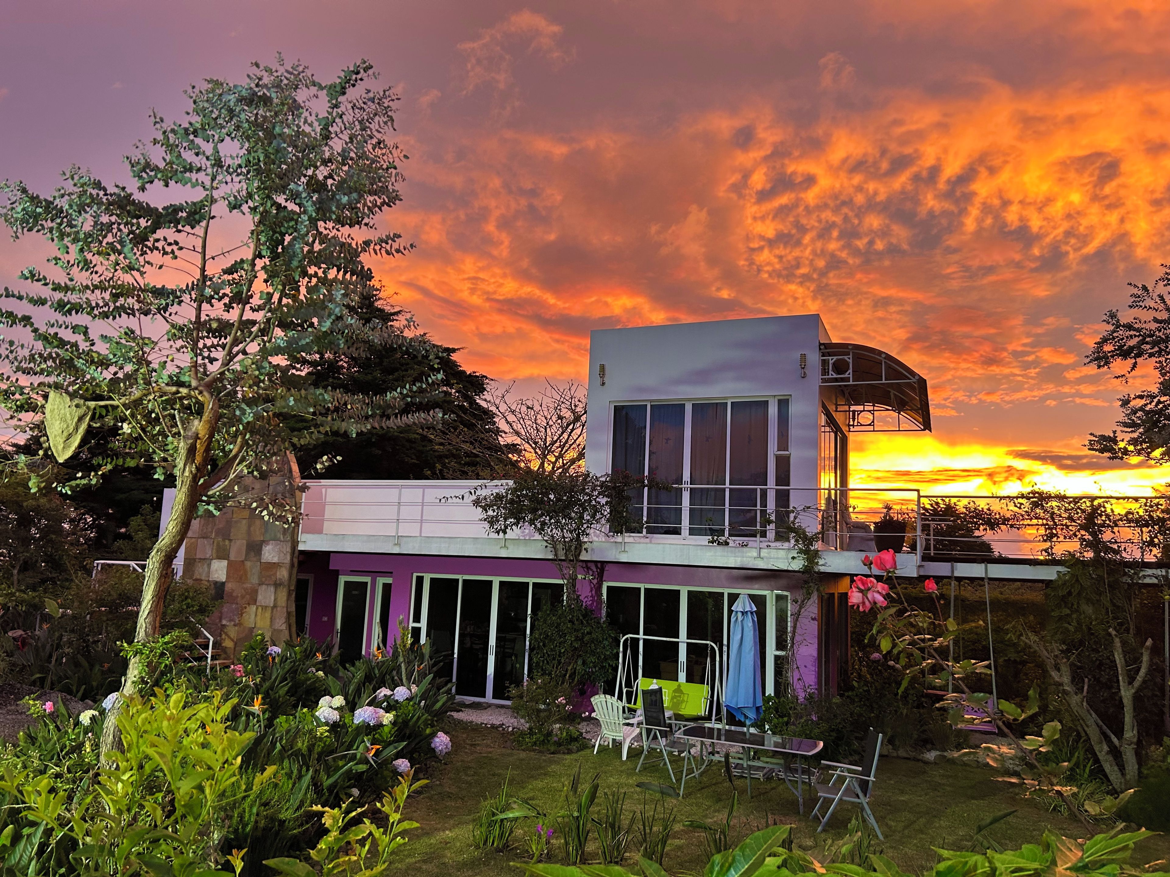 Una casa moderna de dos pisos con un balcón que da a un jardín y una vista al atardecer.