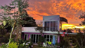 Una casa moderna de dos pisos con un balcón que da a un jardín y una vista al atardecer.