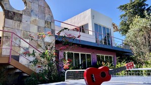 Un edificio moderno con fachada de piedra curva, un balcón con barandilla y una guitarra roja apoyada en una valla.