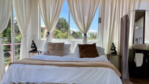 Un dormitorio con una cama grande, dos mesitas de noche, una ventana con cortinas y vistas a zonas verdes.