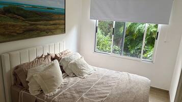 A bedroom with a bed, a window with a view of greenery, a painting on the wall, and a ceiling with a textured finish.