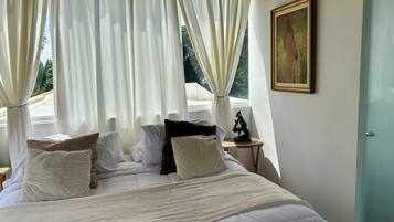 A bed with white bedding, a small bedside table with a sculpture, and a painting on the wall.