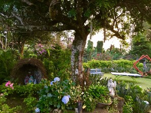 A garden with a variety of plants, a stone structure, and a metal sculpture. - Gosen B&B (San Pablo)