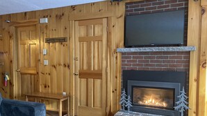 A cozy room with wooden paneling, a fireplace with a brick base, and a flat-screen TV mounted above it. - Sugarloaf Mt. - on the mountain, indoor pool, short walk to lift, quiet (Carrabassett Valley)