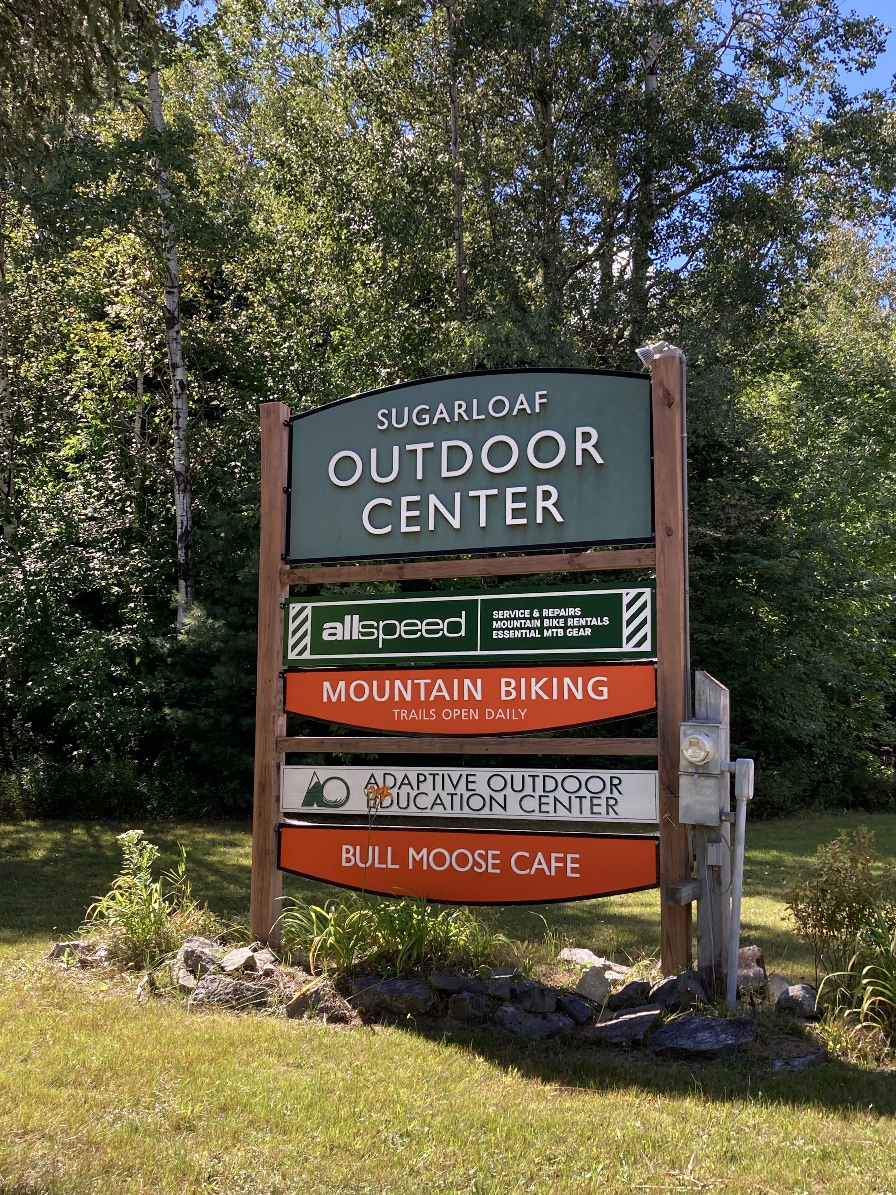 Señal del Sugarloaf Outdoor Center con servicios como ciclismo de montaña, educación ambiental adaptada y un café.