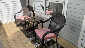 A covered patio with wicker chairs and a table, a bottle of wine, and a window with blinds. - Sugarloaf Mt. - on the mountain, indoor pool, short walk to lift, quiet (Carrabassett Valley)