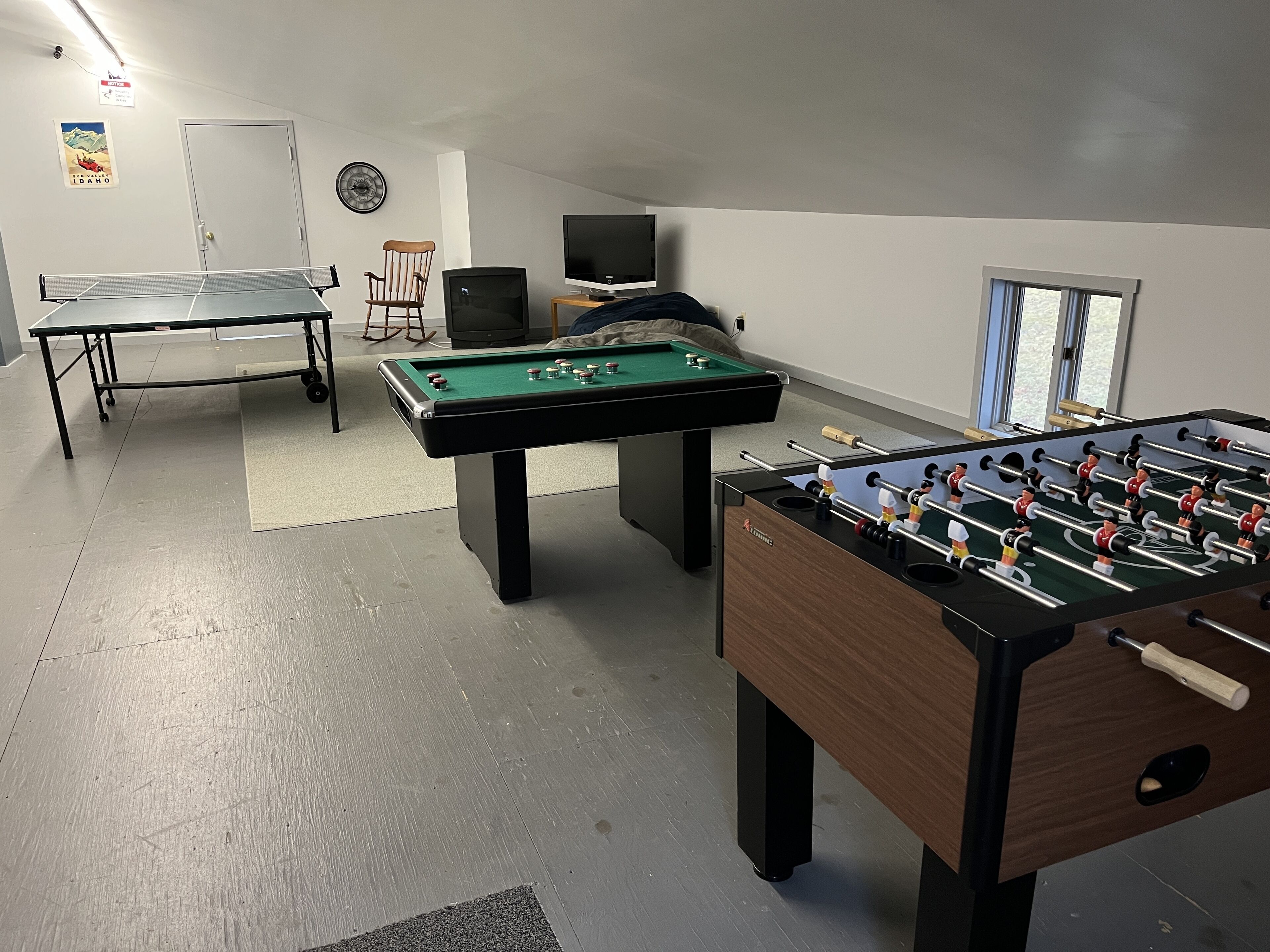 A room with a foosball table, a pool table, and a television.